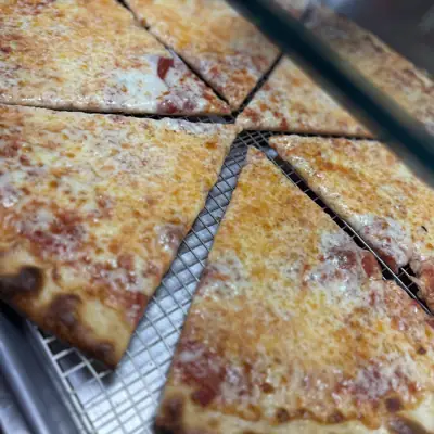 Whole cheese pies cut into slices on the pizza counter